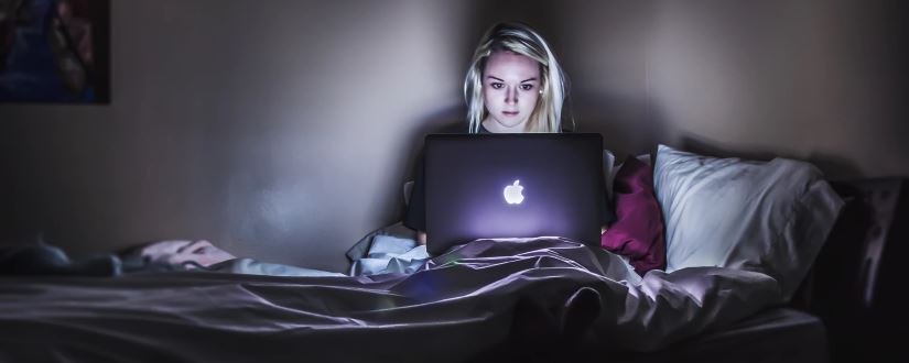 Mujer joven trabajando en cama con un portátil, foto de Victoria Heath, CC0